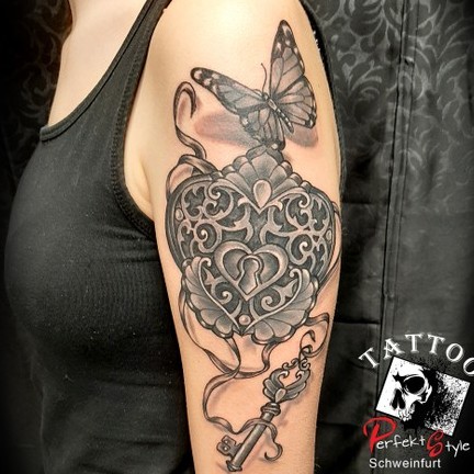 Verziertes Herz-Medaillon mit Schmetterling auf dem Oberarm – Black-and-Grey-Tattoo